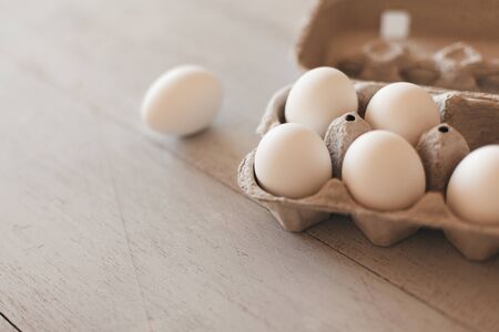 Cardboard egg box with eggs on white wooden table