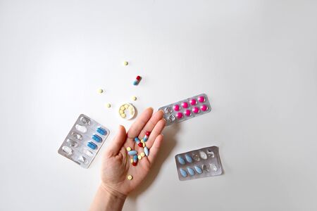 Human hand with a bunch of pills on the palm and some pill in cluster, flat lay on light blue...