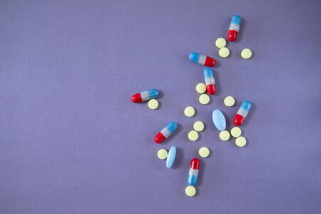 Yellow, blue and red capsules and pills on the light violet background, flat lay with copy space