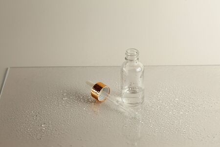 Clear glass bottle with medicine pipette on white background with water drops
