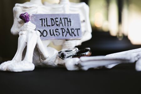 Two white skeletons holding till death do us part sign and two wedding rings