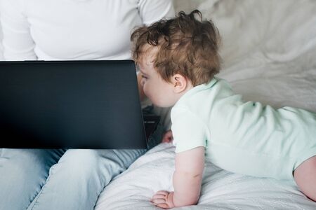 Mother and baby working on the laptop on the bed in bedroom