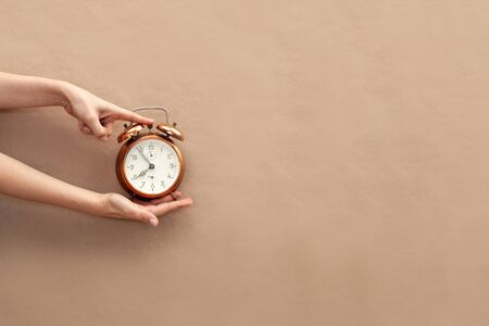 Hand holding bronze watch on brown paper background.