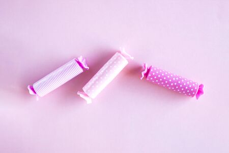 Three candy in polca dot wrapper on pink background.