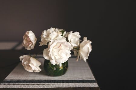 white roses bouquet in glass jar on gray table runner and kitchen tableの写真素材