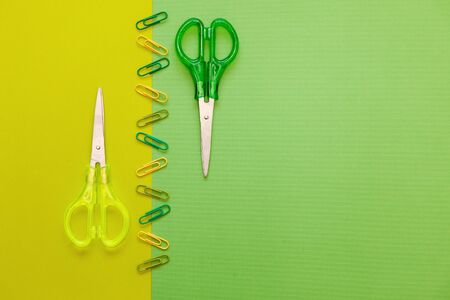 Green and yellow scissors flat lay with paper clips on green and yellow background. Back to school background with copy space. Green and yellow stationary.の写真素材