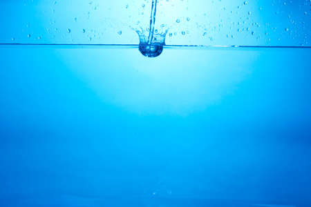 Blue background with water bottle falling in and multiplle drops and splashed. Water bubble textureの写真素材