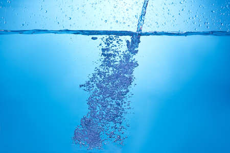 Blue background with water bottle falling in and multiplle drops and splashed. Water bubble texture