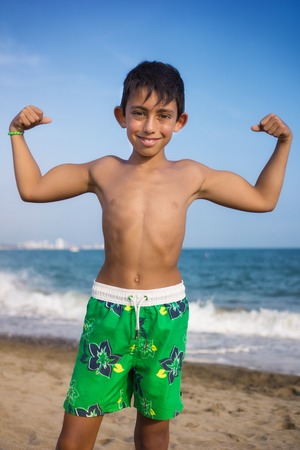 little boy showing his muscles on the beachの写真素材