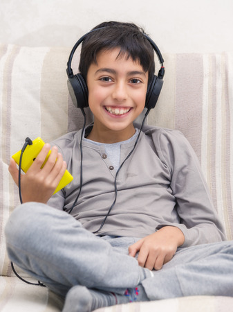 young boy listening music with smartphone and headphoneの写真素材