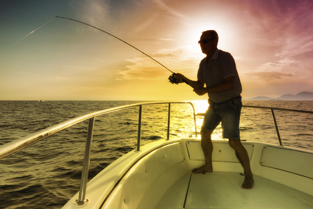 man fishing on the sea from the boat at sunsetの写真素材
