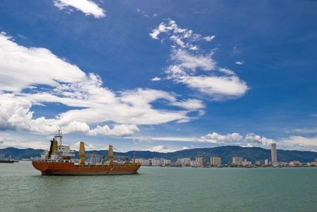 A large red cargo shipping vessel going through a strait and into the port of Penang in Malaysia. の写真素材