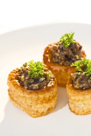 Three vols-au-vent pastries stuffed with a fresh mixture of snails and mushrooms topped with fresh parsley and served on a white ceramic plateの写真素材