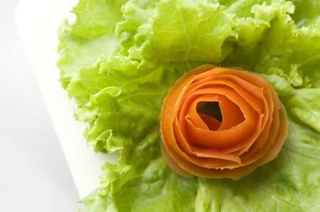 A tomato cut and shaped as a flower on a bed of leaf lettuce served on a white ceramic plateの写真素材