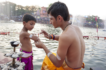 Ujjain, Madhya Pradesh, India - May 18, 2016: A young priest paints the arm of a boy-apprentice before a fire ceremony called Ã¢ï¿½ï¿½aartiÃ¢ï¿½ï¿½ at the Kshipra River during the Kumbh Mela religious festival in Ujjain, India on May 18, 2016. Kumbh Mela のeditorial素材