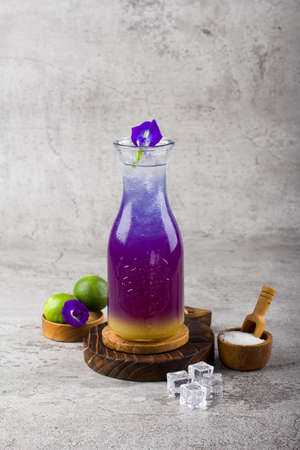 iced butterfly pea flower tea or teh bunga telang with glass bottle on wooden coaster and white background textureの写真素材