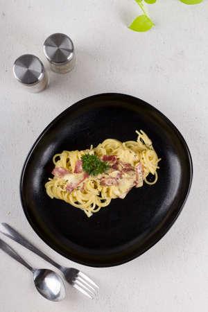 pasta spaghetti carbonara with cream sauce, slice beef, olive oil and fresh green parsley in black oval plate with a pair of cutleries and dark blue napkin with white lineの写真素材