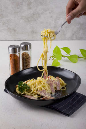 pasta spaghetti carbonara with cream sauce, slice beef, olive oil and fresh green parsley in black oval plate with a pair of cutleries and dark blue napkin with white lineの写真素材