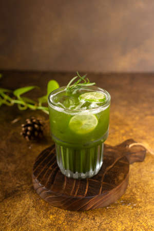 vegetable juice with ice in glass with slice of lemon and rosemary, on rustic wooden tray and authentic backgroundの写真素材