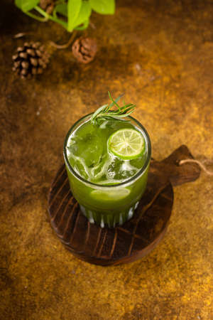 vegetable juice with ice in glass with slice of lemon and rosemary, on rustic wooden tray and authentic backgroundの写真素材