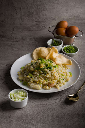 fried rice or nasi goreng kampung, with scrambled egg, spring onion and cracker on white plate