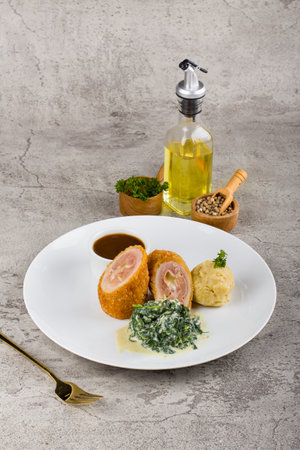 cordon bleu with ham, cheese, cream spinach and smashed potato at white plate on tableの写真素材