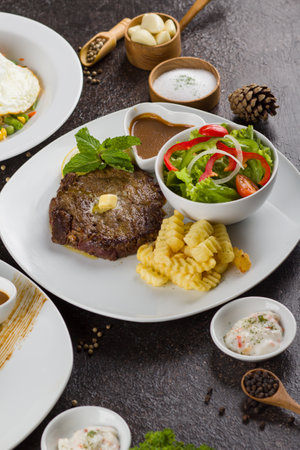 Grilled beef steaks with potato, vegie and steak sauce at white plate on texture rustic tableの写真素材