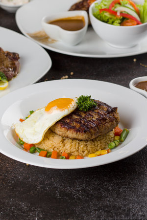 Grilled beef steaks with potato, vegie and steak sauce at white plate on texture rustic tableの写真素材