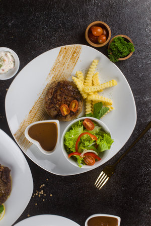 Grilled beef steaks with potato, vegie and steak sauce at white plate on texture rustic tableの写真素材