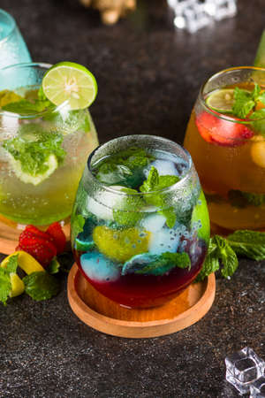 Several cocktail in glass with ice cube, strawberry, lime, ginger and mint leaf on texture tableの写真素材