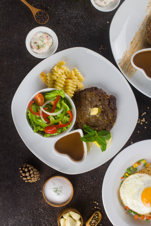 Grilled beef steaks with potato, vegie and steak sauce at white plate on texture rustic tableの写真素材