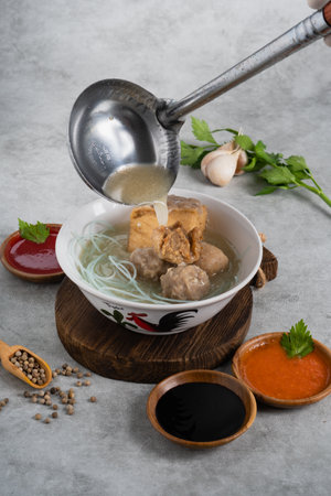 Bakso or indonesian meatball served with broth soup, tofu, noodle and deep fried wonton or dumpling on white bowlの写真素材