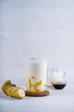 Vegan banana smoothie in plastic cup on white rustic background. Healthy drink