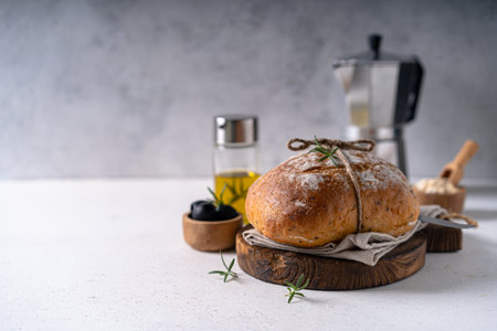 Freshly baked sourdough ciabatta bread with olives and rosemary on a white abstract table. Artisan...