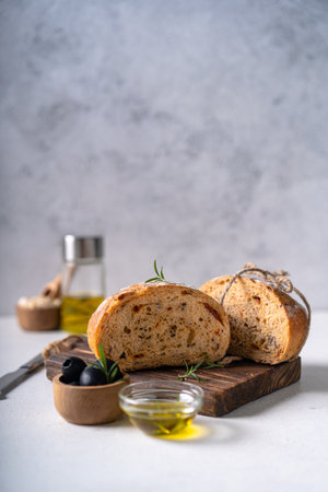 Homemade sourdough ciabatta slice bread with olives and rosemary on a white abstract table. Artisan...