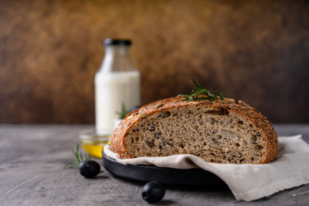 Freshly baked sourdough bread from whole grain flour and pumpkin seeds on a grid, olive oil and black olive on a rustic wooden table. Artisan bread.の写真素材