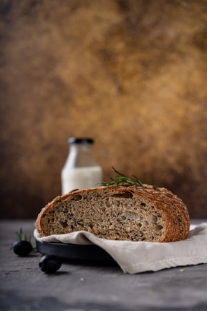Freshly baked sourdough bread from whole grain flour and pumpkin seeds on a grid, olive oil and black olive on a rustic wooden table. Artisan bread.の写真素材