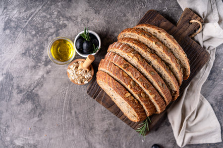 Baked sourdough bread from whole grain flour and pumpkin seeds on a grid, olive oil and black olive...