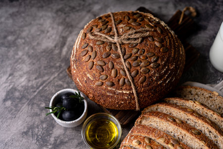 Baked sourdough bread from whole grain flour and pumpkin seeds on a grid, olive oil and black olive on a rustic wooden table. Artisan bread.の写真素材