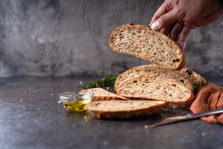 Sliced sourdough bread from whole grain flour and pumpkin seeds on a grid, olive oil and black olive...