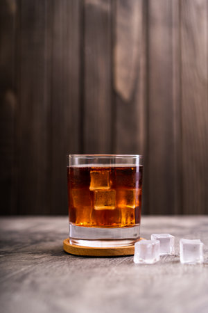 Whiskey, bourbon or cognac on glass with ice cube on a rustic wooden background with copy space