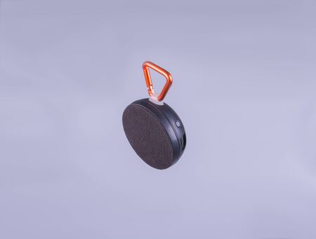 black, wireless speaker with orange carabiner on a gray background side viewの写真素材