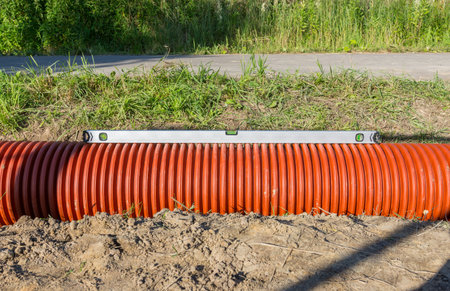 orange corrugated plastic pipe for the entrance lies in a ditch, photo was taken on a sunny summer dayの写真素材