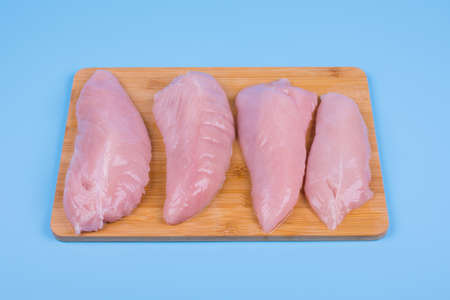 four chicken breasts lie in a row on a wooden board, background blue, top viewの写真素材