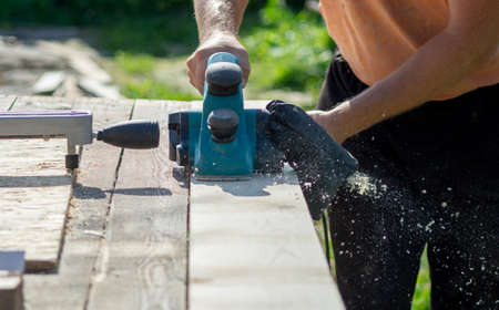 a worker treats a board with an electric plane, the photo was taken on a sunny summer day
