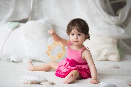 Cute girl, princess, a child in a pink dress on the white bedの写真素材
