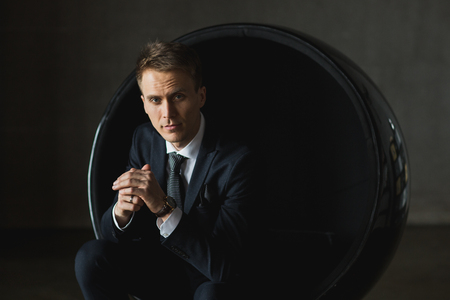 young businessman sitting in chair on grey backgroundの写真素材