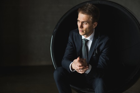 young businessman sitting in chair on grey backgroundの写真素材