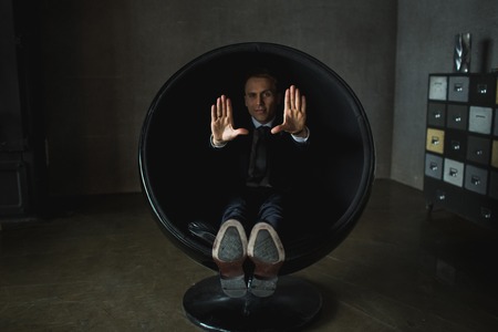 young businessman emotional posing sitting in chair on grey backgroundの写真素材