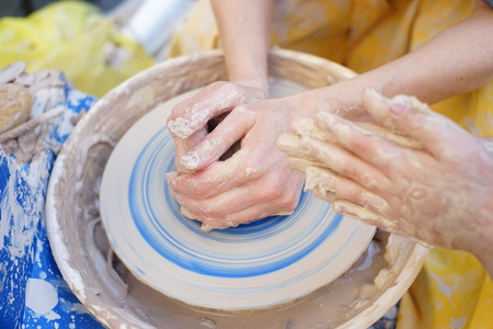 A potters hands guiding a child hands to help him to work with the ceramic wheelの写真素材